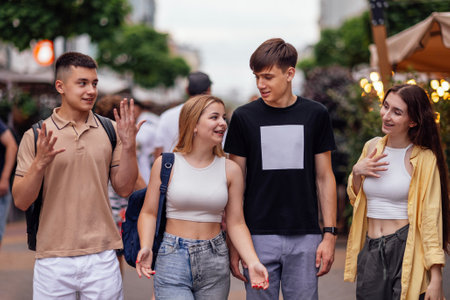 Four friends in casual clothes are walking around the city. Teenagers laugh and have fun. Two guys and two girls outdoors on the street. Happy teens enjoying vacation together.の写真素材