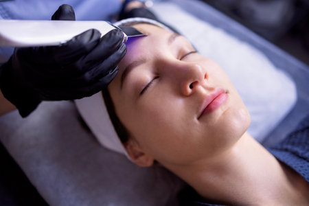 Beauty master makes ultrasonic facial peeling to her client. Young beautiful caucasian woman doing an effective cleansing of the skin and pores in a beauty salon. Electric spa equipment. Copy spaceの写真素材
