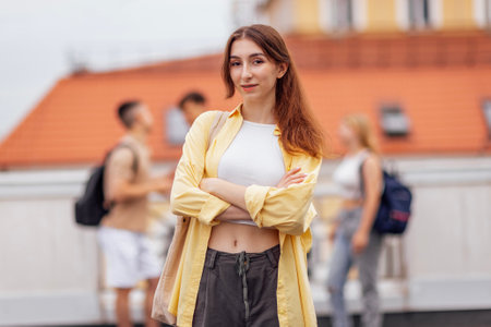 A cute teenage girl in a white top and jeans with a backpack looks at the camera and smiles....