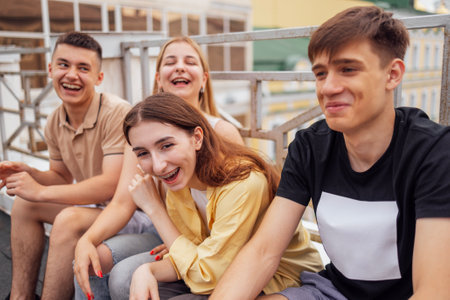 Four teenagers in casual clothes chat and laugh on the roof of the house. Girls and boys have fun together. Funny students relax and walk. Happy friends enjoying vacation together.の写真素材