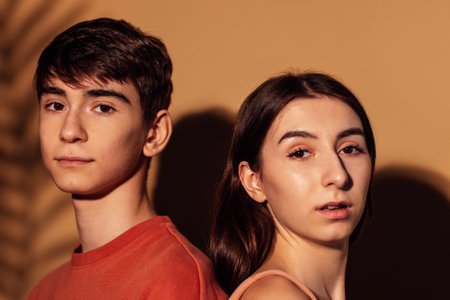 A close-up portrait of a smiling girl with braces and a boy in a gentle embrace. A brother and sister with a beautiful leaf shadow on their faces. Cute teenagers on a beige background.の写真素材