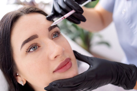 Beauty injections. Female cosmetologist in black gloves makes an injection to her client. Treatment with hyaluronic acid. Introduction of liquid into the skin of woman.の写真素材