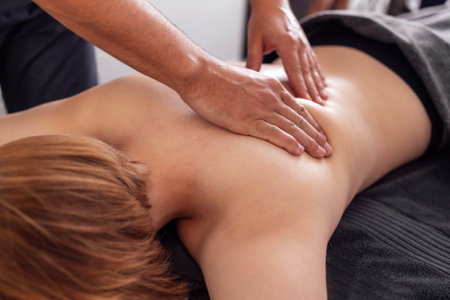 Young caucasian woman getting back massage in spa salon. Strong hands of the masseur touch the female client back. Woman gets relaxation in beauty center or clinic. Copy space.の写真素材