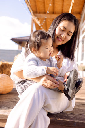 A young Asian woman in white clothes is sitting next to her little daughter. Korean mom and her cute baby in the backyard of the house.の写真素材