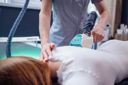 Cosmetician using LPG slimming apparatus on body of female client in white suit lying on couchの写真素材