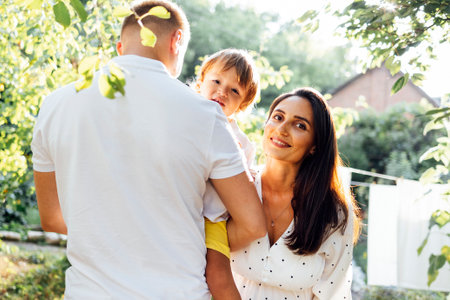 Cute family in light casual clothes in garden on terrace of house. Young couple and their outdoor...