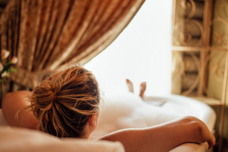 Close-up of a young woman taking a bubble bath. A charming girl relaxes under hot water. The view from the back. Retro vintage interior. Copy space.の写真素材