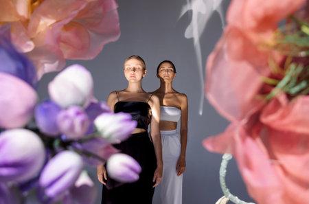 Two young diverse women wearing tops while posing together on floral background. Charming models with natural makeup and perfect skin. Beauty and friendship concept.の写真素材