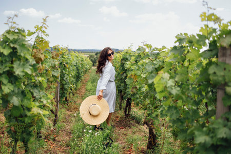 Joyful woman, wearing a hat, in a vineyard in the sun. Holiday and travel concept. Back viewの写真素材