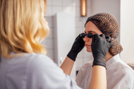 Young woman is covered eyes with special glasses for depilation before hair removal procedure....