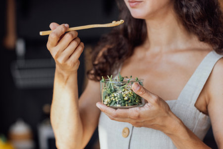 Close-up of a glass bowl with a green salad in a female hands. A young woman eats healthy and delicious herbs and cabbage. Vegan with healthy and vitamin-rich food.の写真素材