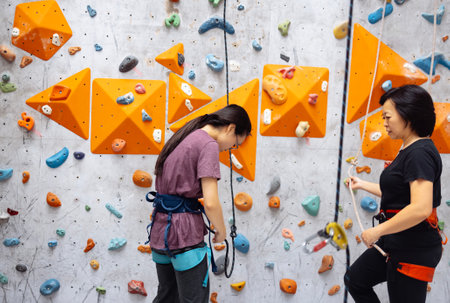 Smiling Asian women in sportswear posing near the bouldering training wall. Mother and daughter on the climbing wall. A cute Korean girl and her parent are working out at the gym.の写真素材