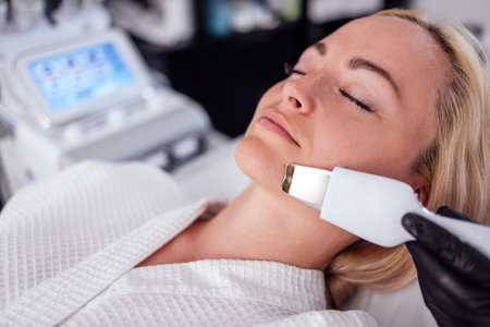 Beauty master makes ultrasonic facial peeling to her client. Young caucasian woman doing an effective cleansing of the skin and pores in a beauty salon. Electric spa equipment. Copy spaceの写真素材