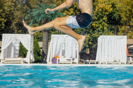 Close-up of a young boy jumping into the pool. A teenager is having fun in clear water. The concept of recreation, entertainment and vacations. Copy space.の写真素材