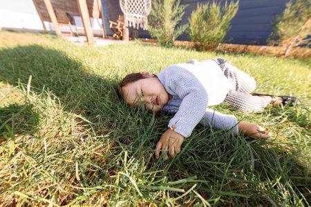Asian sweet girl is lying on a green lawn. A cute Korean baby sleeps on the grass in the backyard of the house. A little kid in casual clothes is playing in a meadow.の写真素材