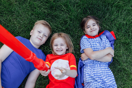 Children lie and laugh on the green lawn. Cute kids have fun outdoors in the meadow. Little friends in casual clothes have a great time together.の写真素材