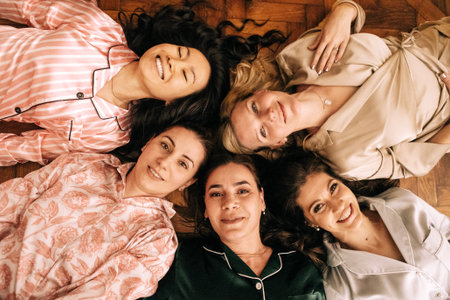 Young smiling women in pajamas are lying on the floor. Charming multiethnic friends at a house...