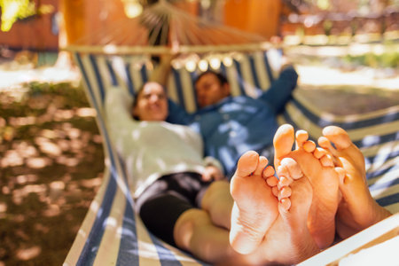A young married couple is relaxing in the backyard of the house. An attractive husband and wife are lying in a hammock outside. A happy family spends time together and enjoys their holidaysの写真素材