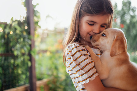 Close-up portrait of a little girl hugging a puppy. A cute small kid is playing with a dog. A sweet child is happy with her pet. A lovely preschool girl takes care of the labradorの写真素材