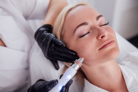 Young woman lies with her eyes closed during hardware moisturizing of the facial skin. The blonde...