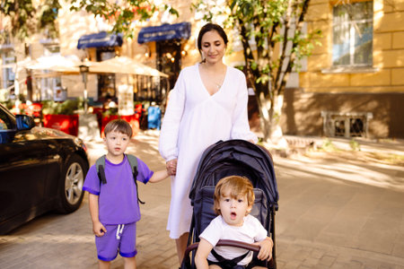 Pregnant woman in white dress walks with her two children around the city. Young mother and her sons...