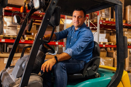 A young attractive forklift truck driver in a warehouse of goods. A handsome worker in casual clothes on a self-propelled cargo truck. A man in a car in a product storage shopの写真素材
