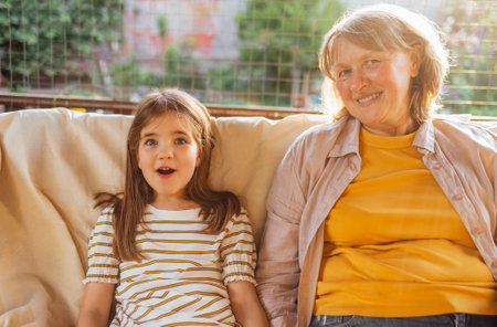 Smiling mature woman and her sweet granddaughter in backyard of house. Laughing grandmother hugs her little granddaughter. Pensioner and child are relaxing together in the garden. Happy family outdoorsの写真素材