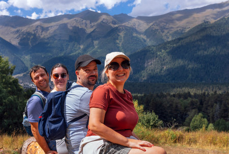 A group of tourists is sitting on a log and enjoying the mountain scenery. Happy friends with...