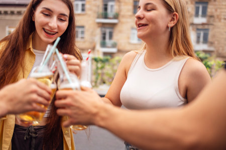 Group of teenagers are having fun and drinking lemonade on the street. Cute friends raise toast and...
