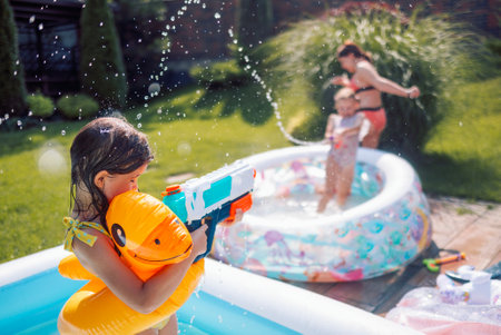Joyful little girl in swimsuit with inflatable circle on terrace. Cute kids are messing around and splashing water in the backyard of the house. Carefree children have fun in pool in summer outdoorsの写真素材