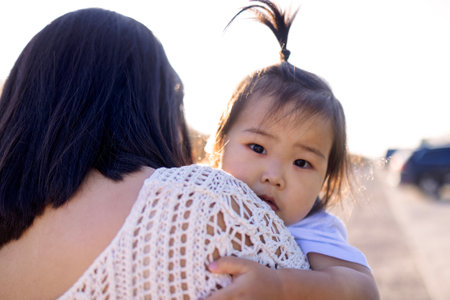 A young Asian woman hugs her little daughter. An attractive mom walks with her cute girl outdoors. Happy Korean family in the park.の写真素材