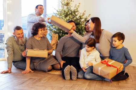 A big happy family gives gifts under the Christmas tree at home. Parents, grandparents, children and grandchildren celebrate Christmas together. Laughing people exchange holiday present boxes.の写真素材