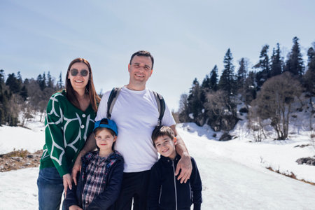 A happy family on vacation in the mountains. Cute little children and their parents in casual clothes against a snowy landscape. Dad, mom, daughter, and son are traveling togetherの写真素材