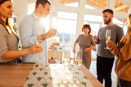 Smiling people raise glasses of champagne in dining room of house. Married couples of different ages celebrate Christmas Eve. Big happy family and friends are meeting together. House party.の写真素材