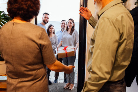 A mature couple greets their smiling guests at home. Laughing adult children came to their parents with gifts. Happy people spend family holidays together. Modern cozy home interior.の写真素材