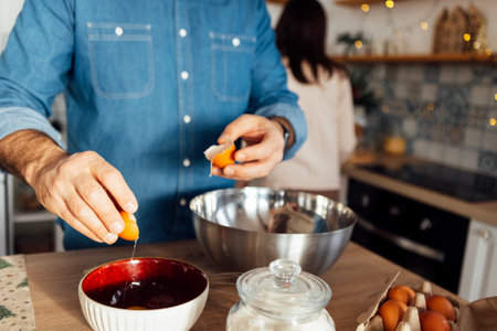 A young handsome man cooks in the kitchen at home. An attractive man breaks eggs into a metal bowl....