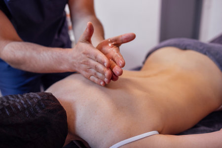 Massage therapist gives a back massage to his female client in a spa salon or clinic. Close-up of the male hands with oil on them. Health, relaxation and rest concept.の写真素材
