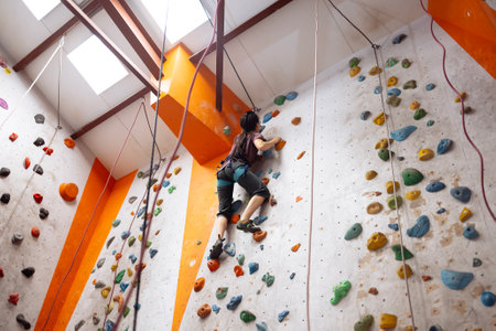 A young Asian woman on a climbing wall. A Korean girl climbs a bouldering wall. Attractive professional sport climber woman having training in the gym. Charming brunette having active time.の写真素材