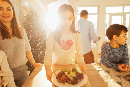 A cute teenager holds a plate of potatoes and salad in the dining room. A happy family cooks Christmas dishes together. Children and parents have lunch at home. Cozy interior with Christmas tree.の写真素材