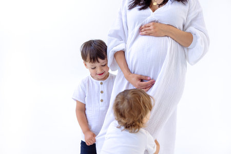 Close-up of the arms and belly of a young pregnant woman and her sweet sons. Little boys hug their...