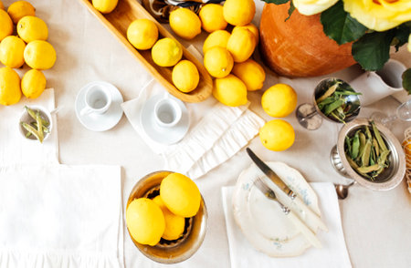 Close-up of vintage plates with fresh and juicy lemons. Kitchen utensils on the table with a white tablecloth. A clay pot with a houseplant. Retro rustic styleの写真素材