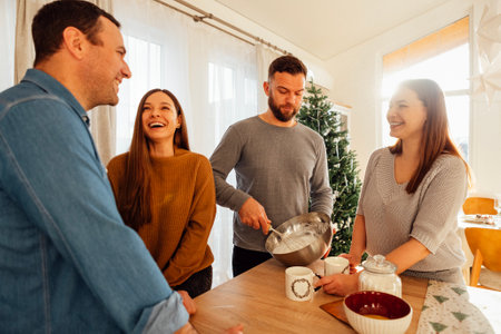 Cute happy friends in sweaters laugh and cook together in the kitchen at home. Smiling young women and men are chatting and having fun at home in the dining room. Cozy interior with Christmas decor.の写真素材