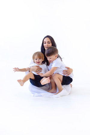 A young pregnant woman in a white dress with her cute sons. Adorable mom and her little kids are playing on the floor. White isolated background. A happy familyの写真素材
