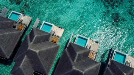 Aerial view of luxurious overwater villas with thatched roofs. The houses are surrounded by clear turquoise water. The wooden walkways connect the bungalows. A serene and exotic escapeの写真素材
