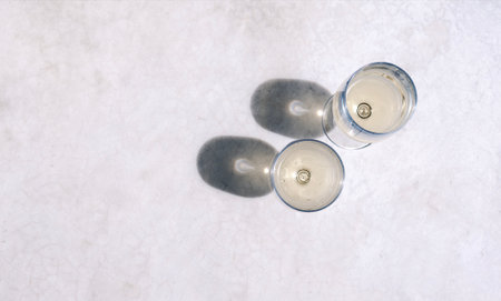 Two elegant long-stemmed glasses with chilled alcoholic beverages on a marble table. Top view....