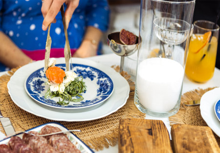 A waiter serves fresh salmon salad onto a blue-decorated plate for a guest. The table is decorated...