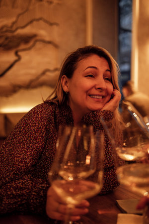 A young woman raising a glass of champagne at a festive table. A laughing blonde makes a toast with...