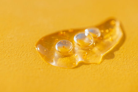 Extremely close-up view of a transparent gel with bubbles and colloidal gold. A drop of moisturizing serum or essence on a bright yellow background. Minimalismの写真素材