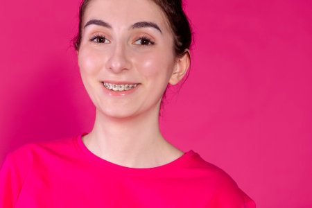Close-up portrait of a young girl smiling on a pink background. Cute teen with braces is laughing on a bright backdrop. A female teenager in a pink T-shirt poses and has funの写真素材