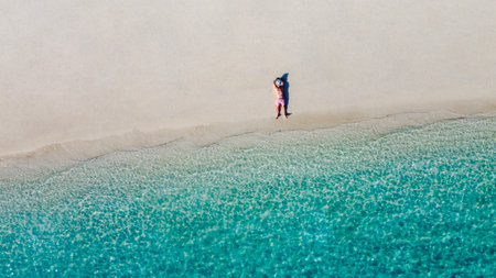 An aerial view of a young man in a white hat on the ocean shore. A man enjoys the seascape. A man is relaxing on a clean sandy beach. Vacation and travelの写真素材